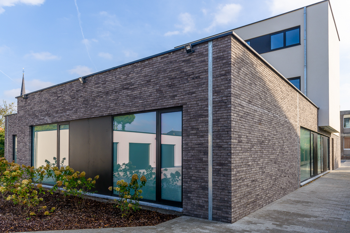 De zwarte aluminium ramen in combinatie met de lichtgrijze gevelsteen zorgen voor een karaktervolle uitstraling Achterkant moderne nieuwbouw voor medisch centrum in Ternat