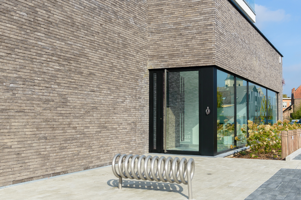 Aan de inkom werd een fietsrek geïntegreerd in de oprit voor een optimale beleving van de klanten Detail inkom met fietsrek moderne nieuwbouw voor medisch centrum in Ternat