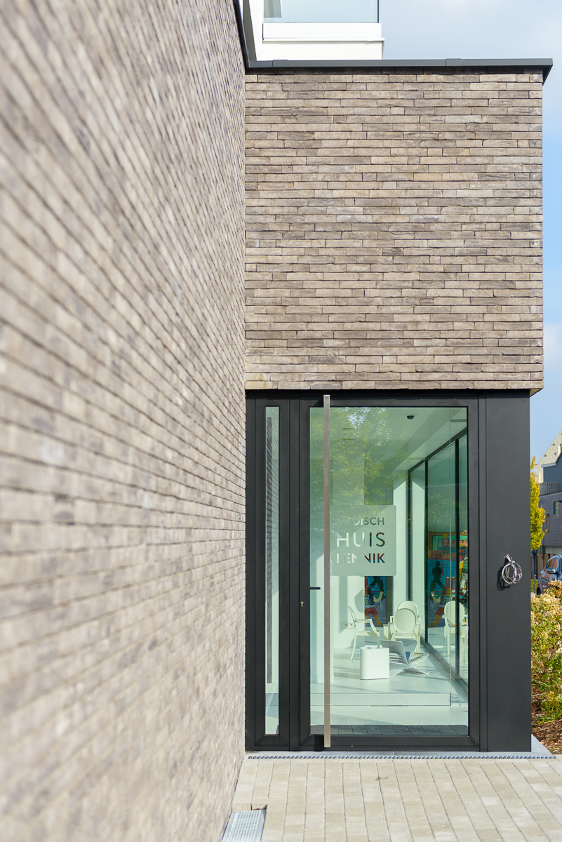 De lichtgrijze gevelsteen bevordert het strakke uitzicht van dit commercieel pand Detail deur inkom moderne nieuwbouw voor medisch centrum in Ternat