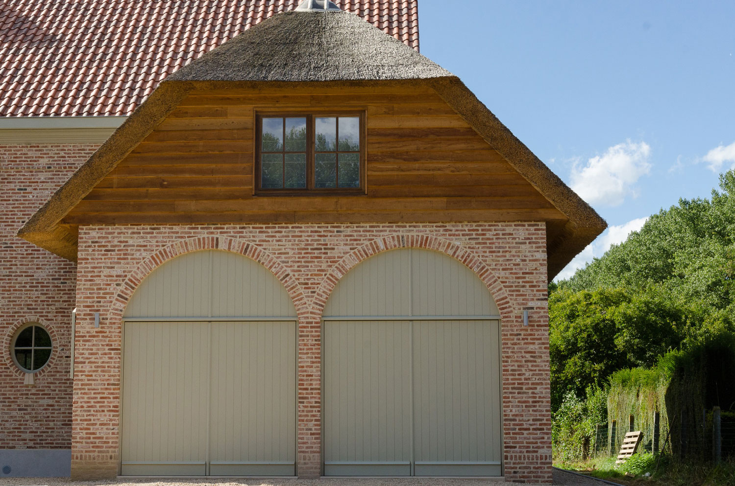De dubbele poort met zijn specifieke bogen en houten en rieten accenten geven een sfeervolle look aan deze woning Detail houten accenten voorgeven en dubbele poort karaktervolle, landelijke nieuwbouw